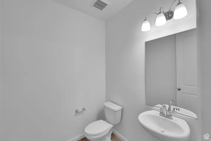 Pedestal sink with chrome faucet, illuminated by a three-bulb vanity light fixture