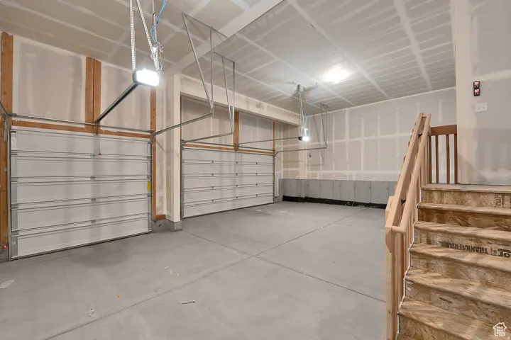 Spacious two-car garage featuring a concrete floor, two individual garage doors, and a partial staircase with wooden railings