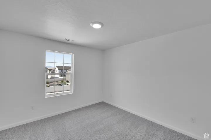 Spacious room featuring light gray carpeting, neutral wall paint, a double-hung window with grilles, recessed ceiling lighting, and baseboard trim