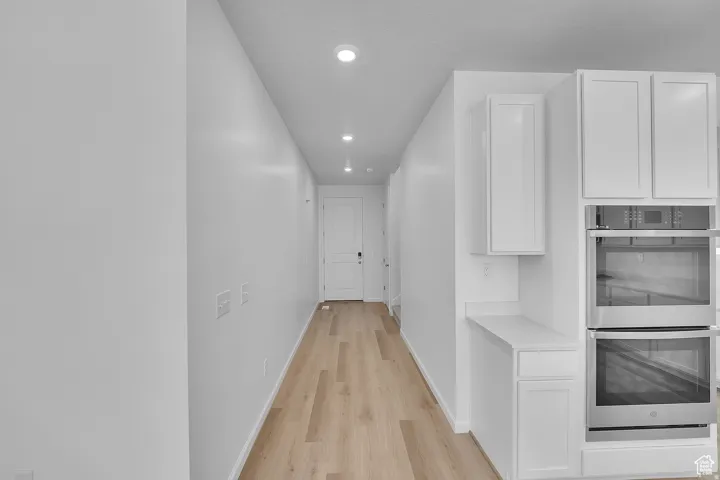 Contemporary hallway with light wood-finish flooring, recessed ceiling lighting, and a white entry door