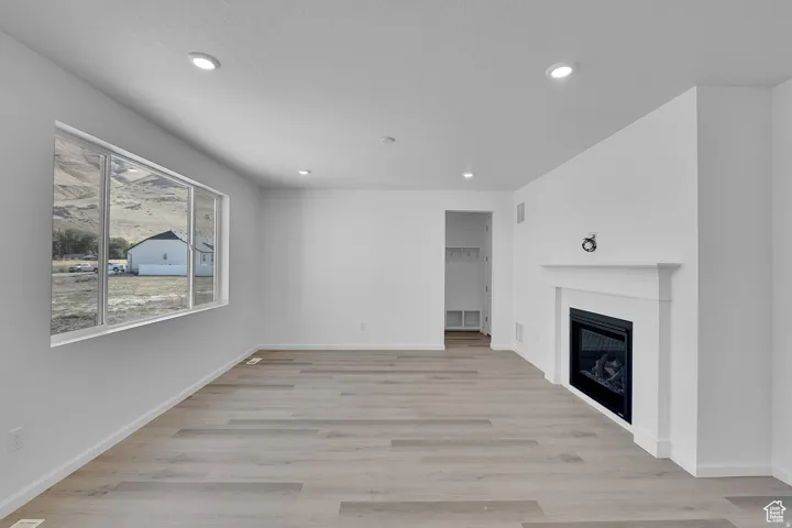 Spacious interior featuring a large picture window, a built-in electric fireplace with a white mantel, recessed lighting, and wood-finish flooring