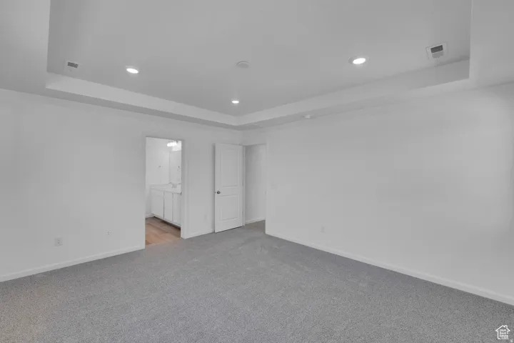 Spacious room featuring light gray carpeting and a tray ceiling with recessed lighting