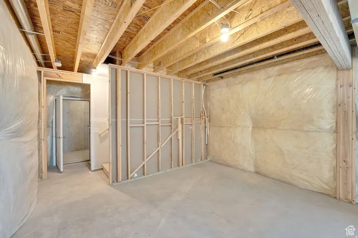 Unfinished basement with exposed ceiling joists and subflooring, concrete flooring, and framed interior walls