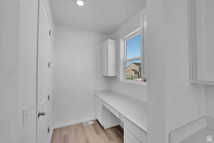 Bright interior space featuring a built-in desk with white cabinetry, a single window, recessed lighting, and wood-finish flooring