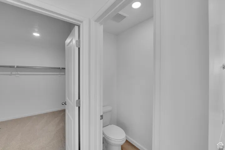 Full-sized white toilet, overhead recessed lighting, and wood-finish flooring