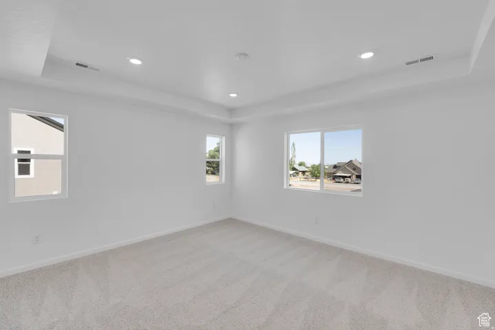 Spacious room featuring new carpet, crisp white walls, multiple windows, recessed lighting, and a tray ceiling