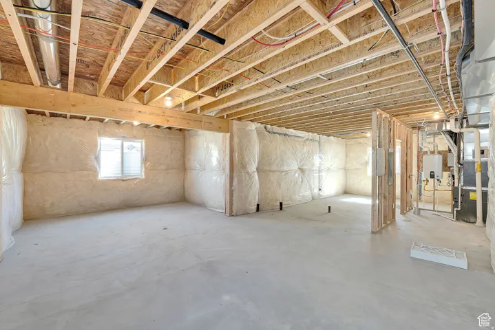 Unfinished basement featuring exposed wood joists, concrete flooring, insulated walls, and a visible window opening