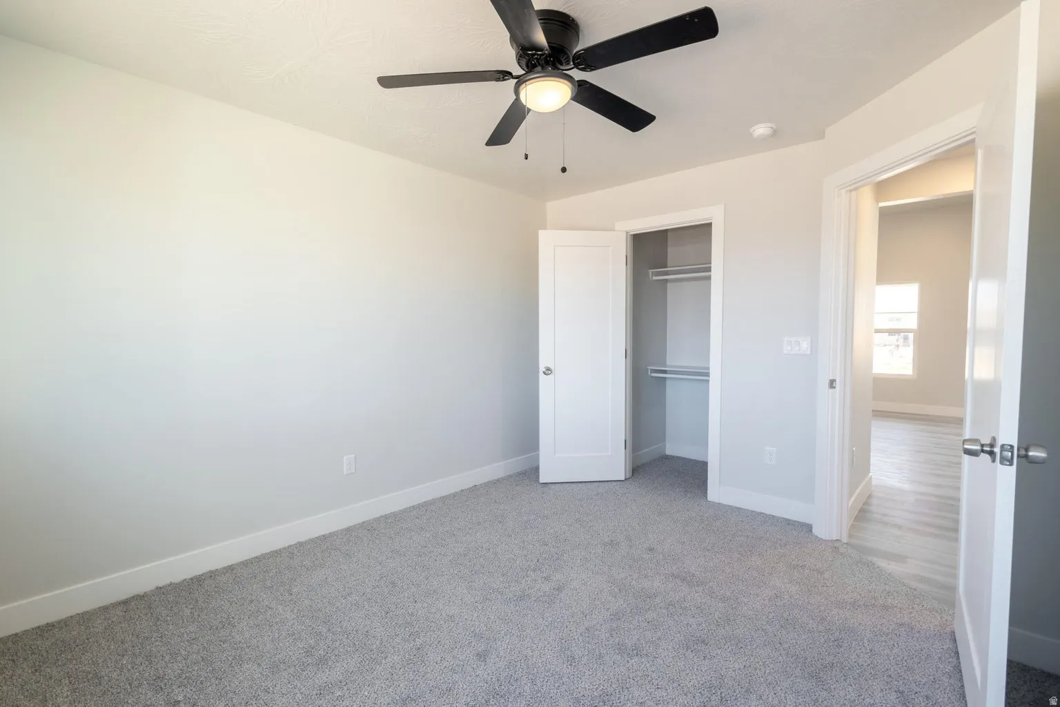 Spacious room featuring light gray carpeting, a built-in closet with shelving, a ceiling fan with integrated lighting, and white trim