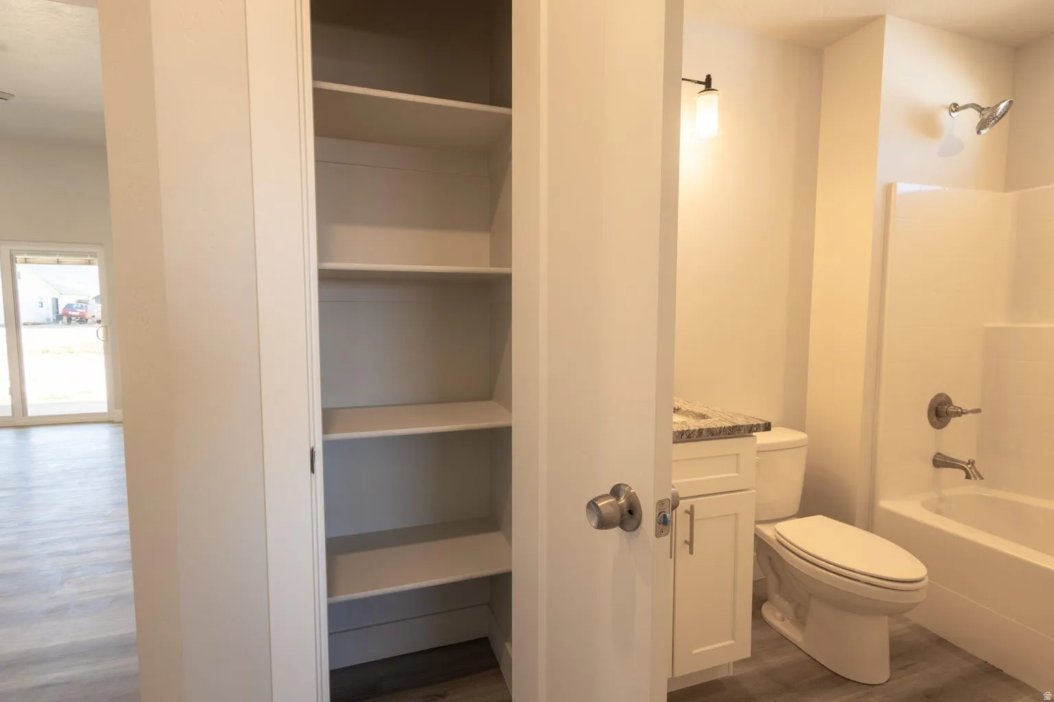 Built-in linen closet featuring multiple shelves, a single vanity with a stone-finish countertop, white cabinetry, a toilet, and a bathtub with shower fixture