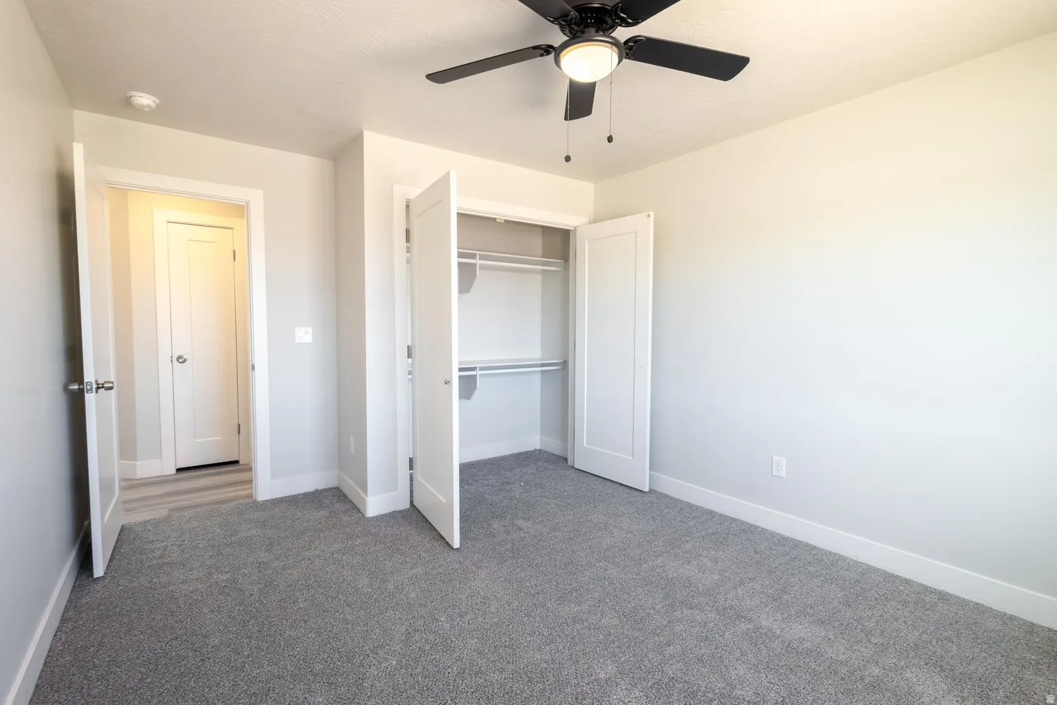 Carpeted room featuring a ceiling fan with integrated lighting, a bi-fold closet with shelving and hanging rods, and modern trim work