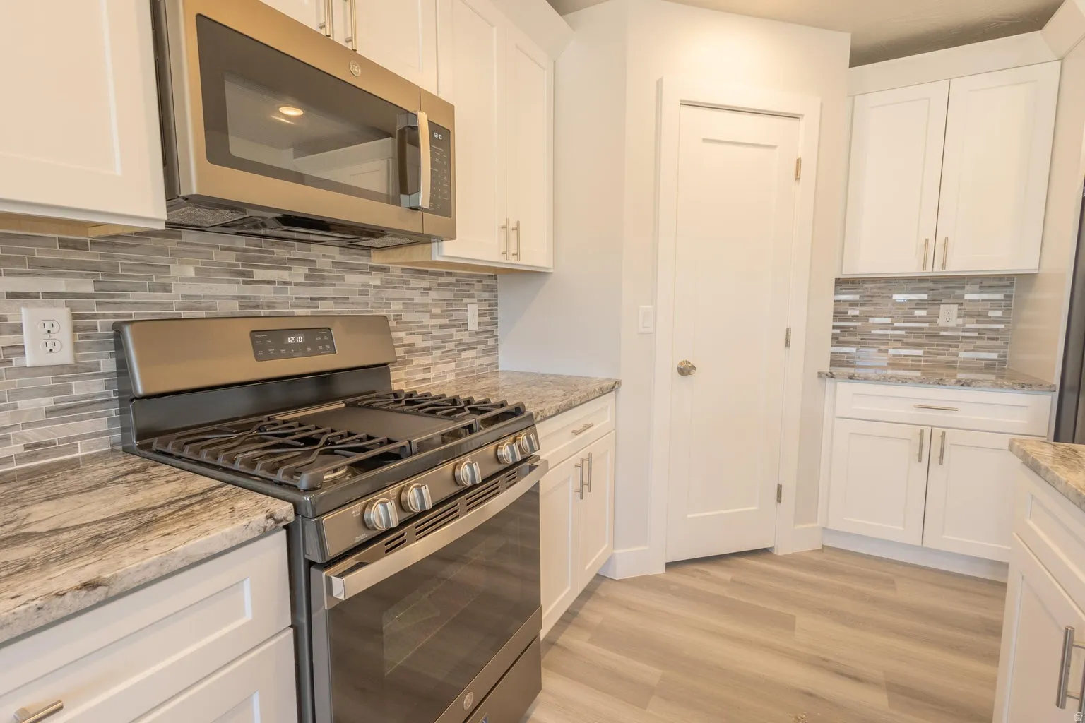 Kitchen featuring stainless steel appliances, white cabinetry, a tiled backsplash, wood-finish flooring, and light-toned countertops