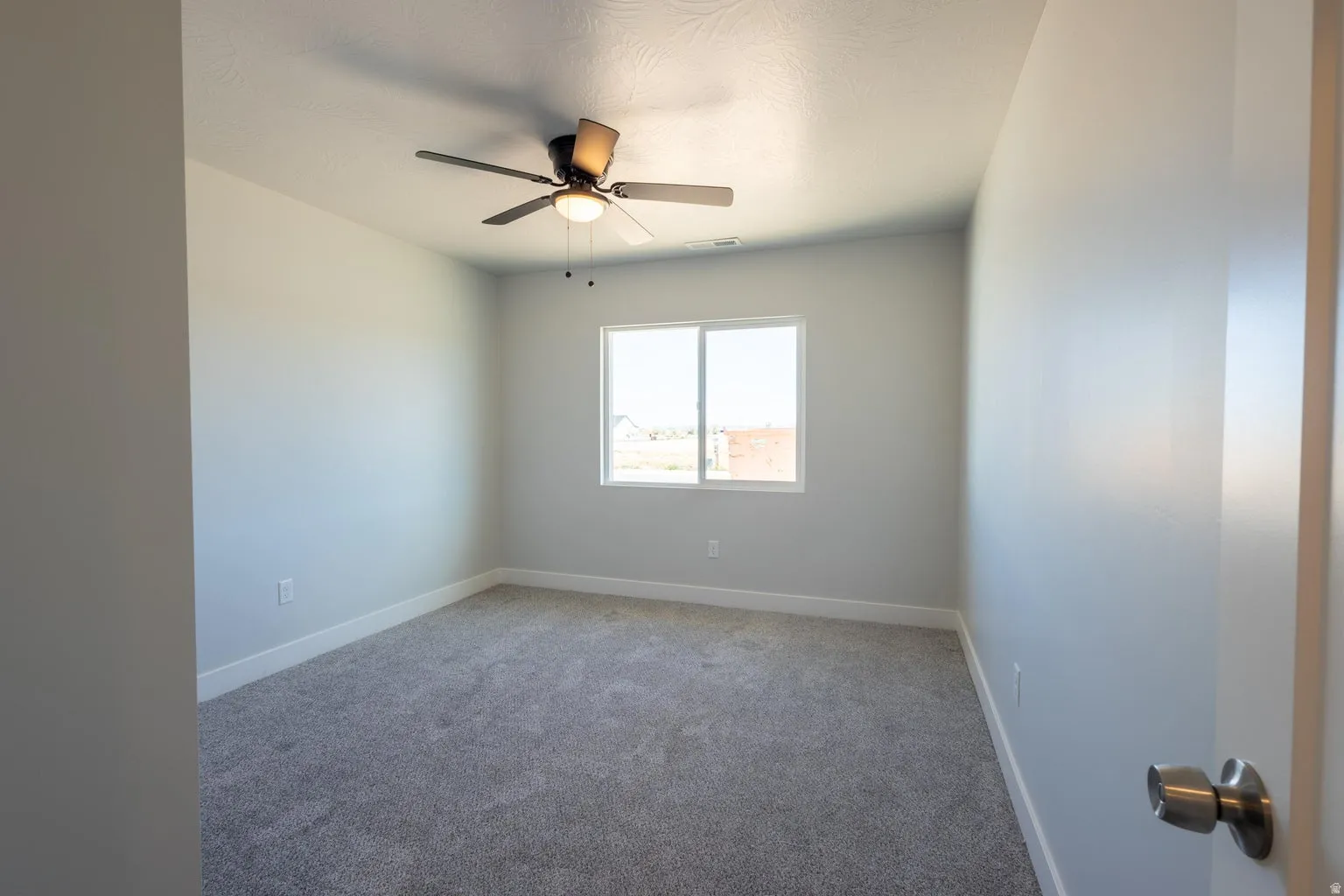 Bright room featuring a ceiling fan with integrated lighting, a large window, light gray walls, white baseboards, and gray textured carpet