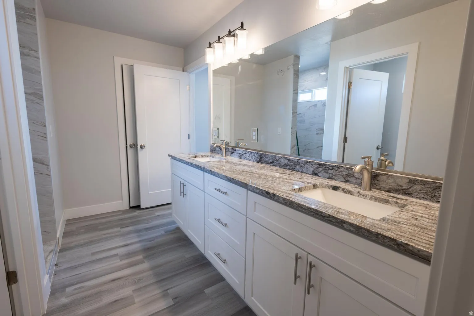 Double vanity featuring dual undermount sinks, stone countertop with integrated backsplash, and brushed nickel faucets