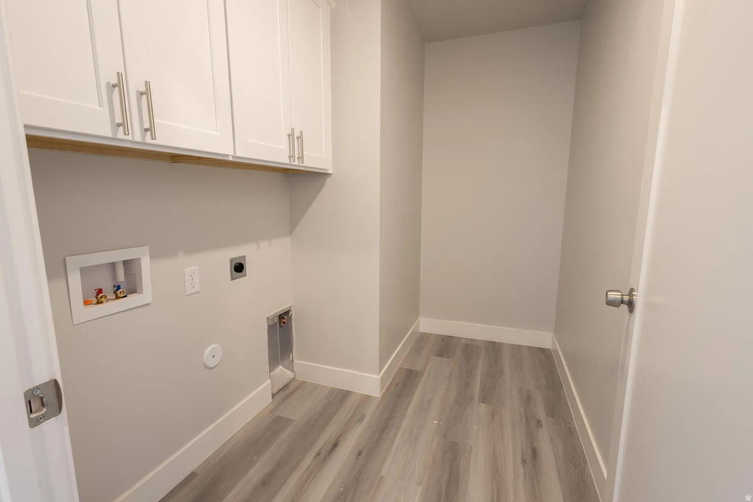 Dedicated laundry area featuring white shaker-style cabinetry with brushed nickel hardware, a wood-finish countertop, and wood-finish flooring