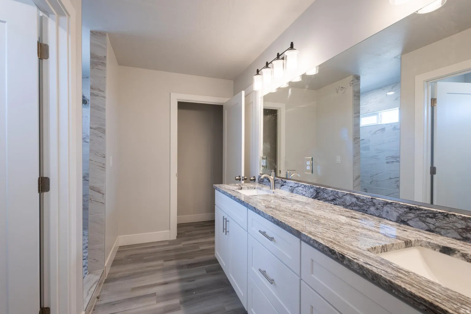 Dual vanity featuring white shaker cabinetry, polished chrome hardware, and a stone countertop with integrated sinks
