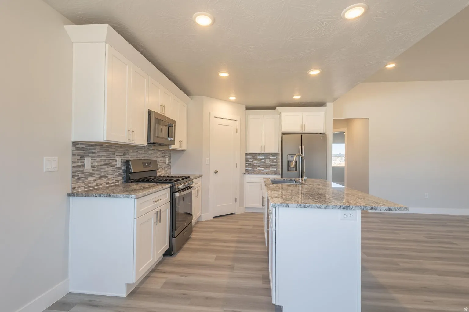 Modern kitchen featuring white cabinetry, a large center island with a stone countertop, stainless steel appliances, and wood-finish flooring