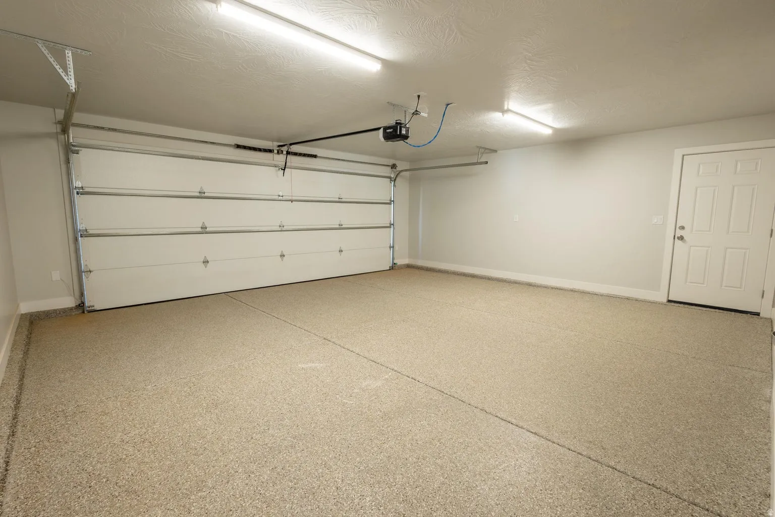 Spacious garage featuring a durable epoxy floor coating, white overhead door, interior access door, and overhead lighting
