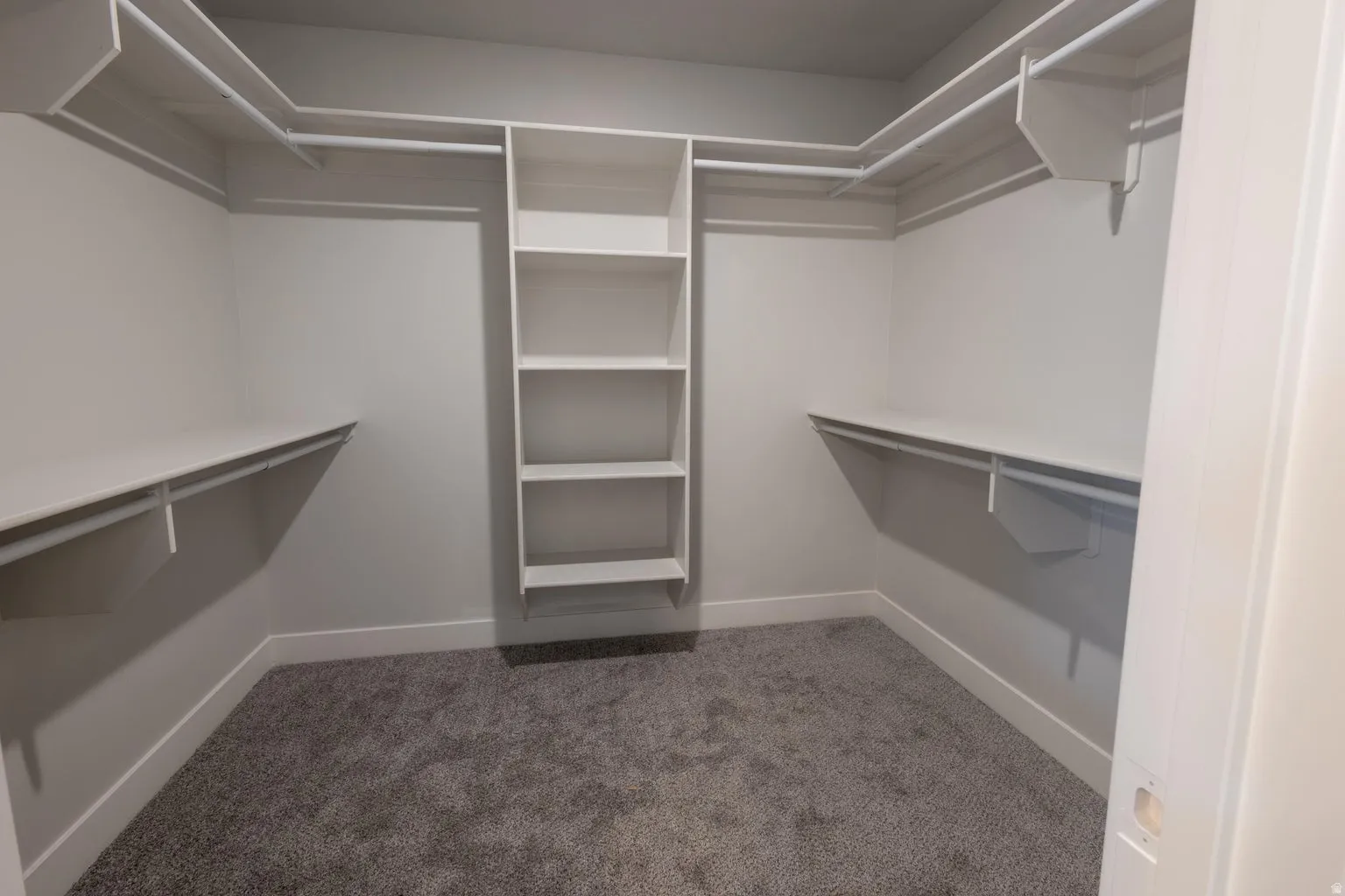 Walk-in closet featuring built-in shelving, hanging rods, and grey carpet flooring