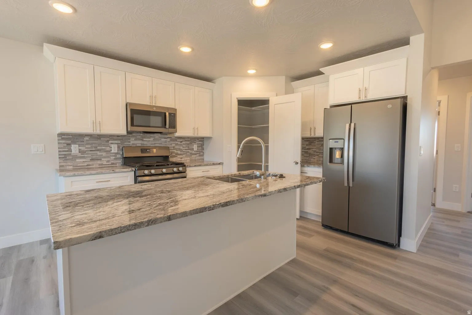 Kitchen featuring a large island with a stone-finish countertop, white cabinetry, stainless steel appliances, a tiled backsplash, and wood-finish flooring