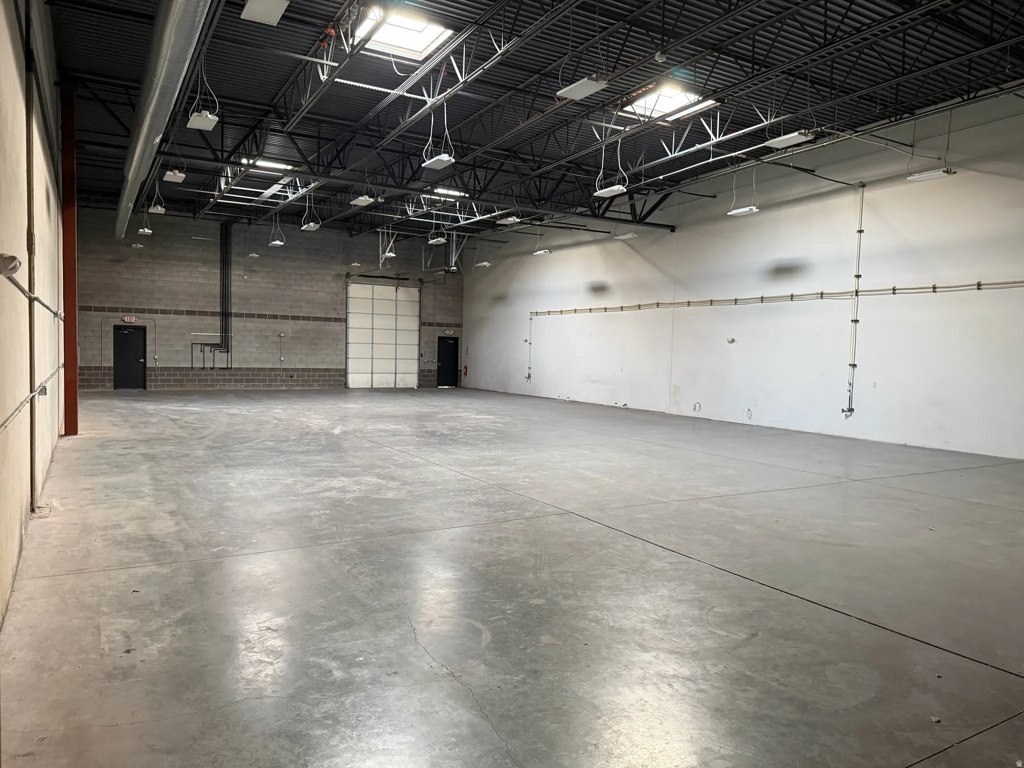 Spacious commercial warehouse featuring an overhead garage door, two entry doors, and durable concrete flooring