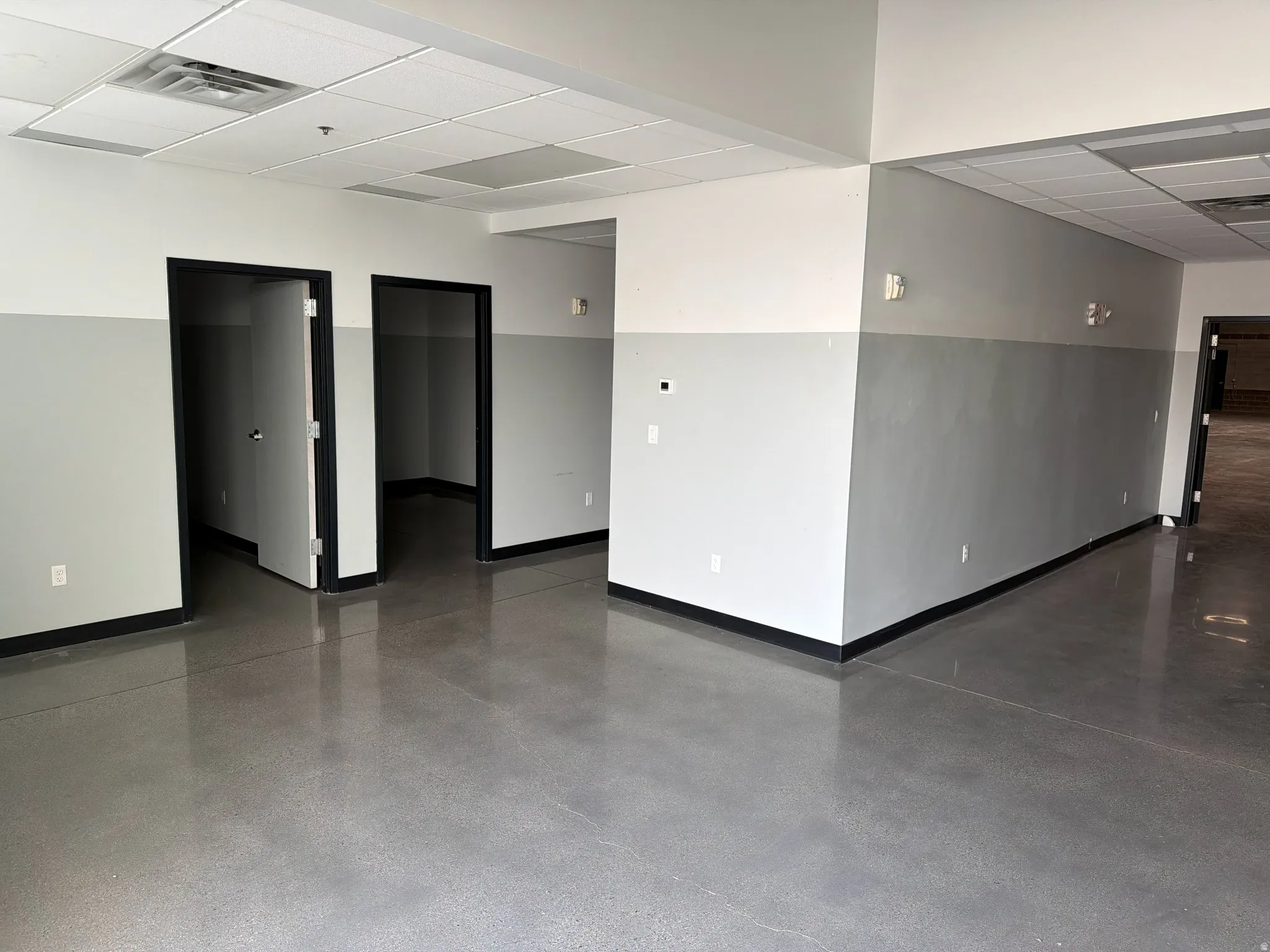 Expansive interior space featuring polished concrete flooring, white and gray two-tone wall finishes, and a drop ceiling with recessed lighting