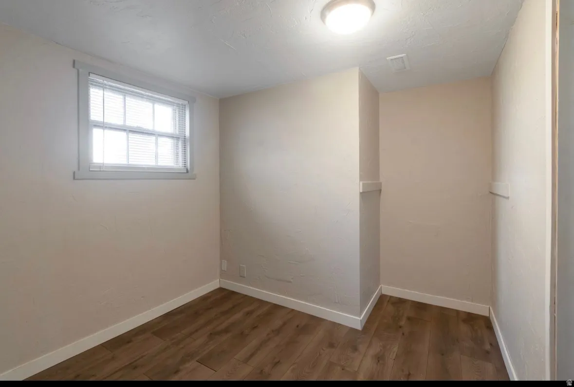 Neutral-toned room featuring a double-hung window with blinds, wood-finish flooring, white baseboards, and a flush-mount ceiling light