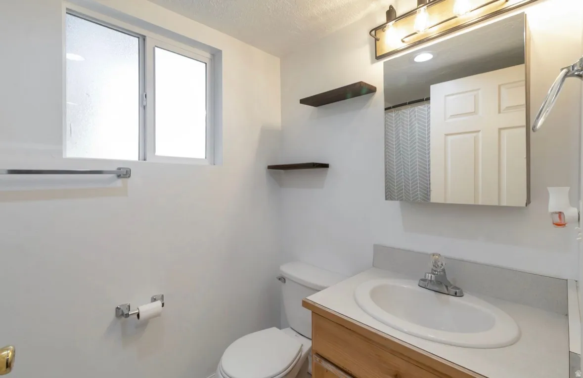 Bathroom with a single vanity featuring a wood-finish cabinet, integrated sink, and laminate countertop