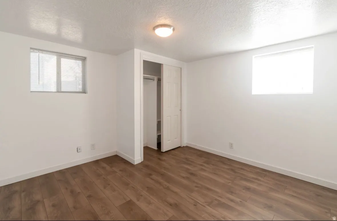 Room featuring wood-finish flooring, two windows, a built-in closet with bi-fold doors, and a ceiling-mounted light fixture
