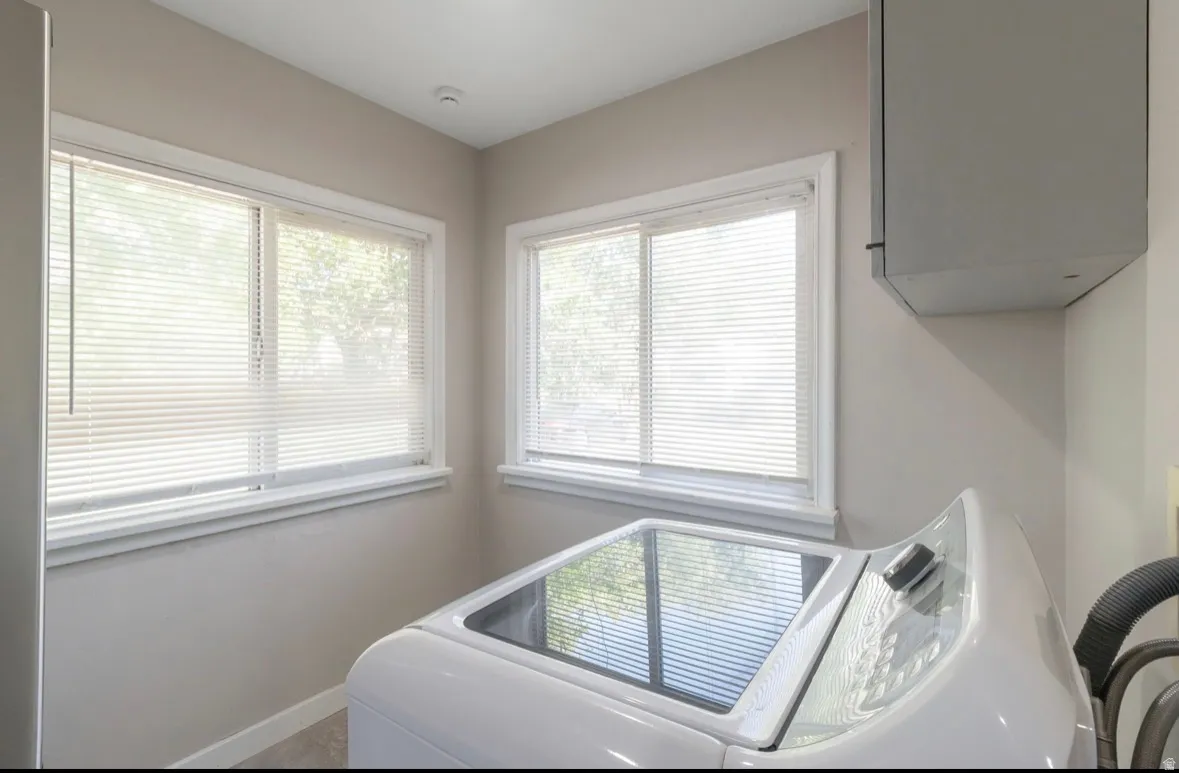 Laundry area featuring two windows with white blinds, neutral wall paint, white baseboards, and a built-in wall cabinet