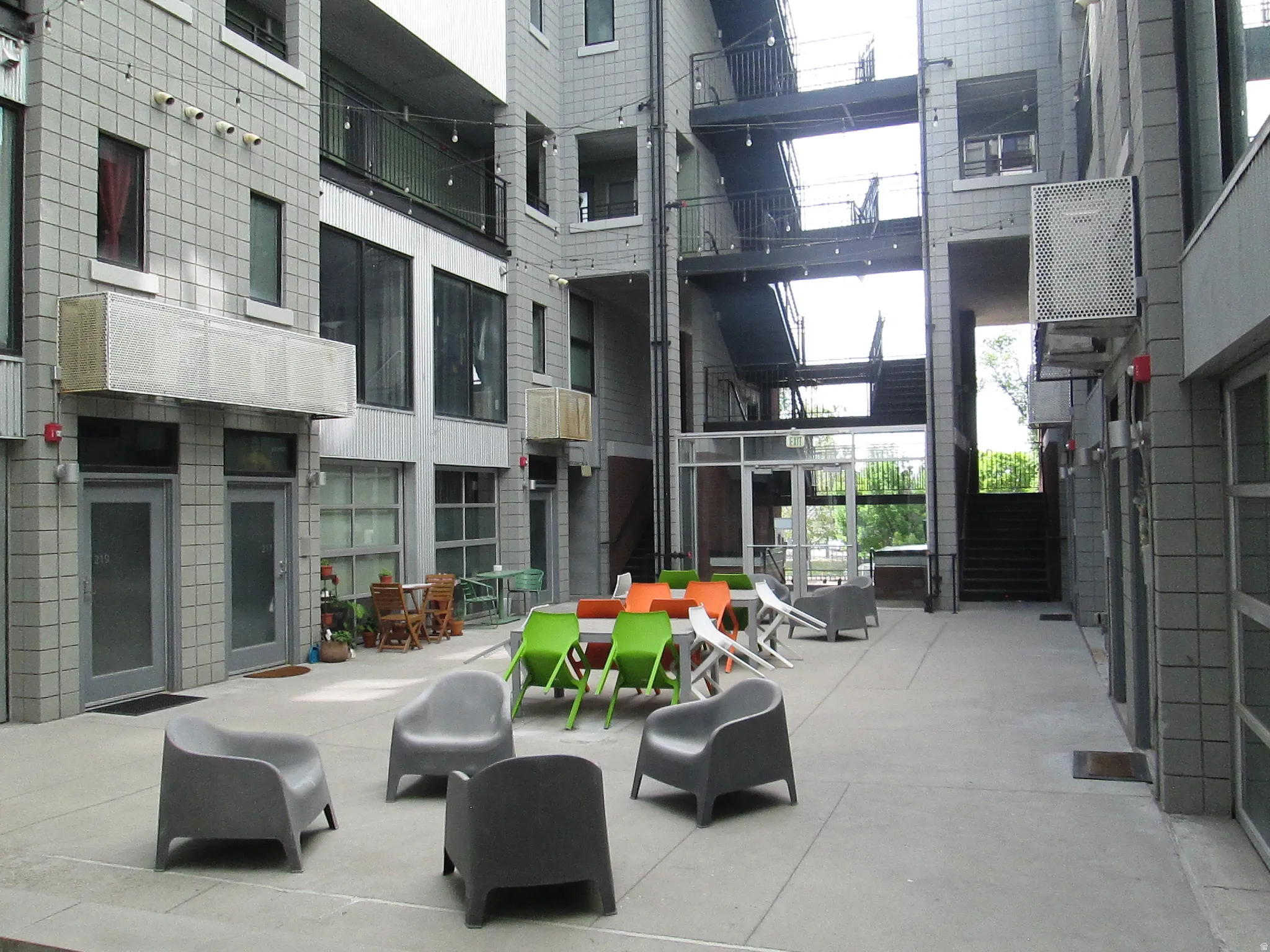 Expansive concrete courtyard surrounded by multi-story buildings featuring a mix of grey tile and corrugated metal siding