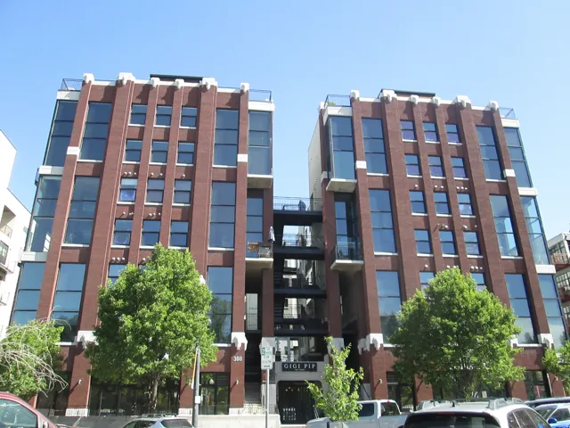 Brick facade building with large, multi-story window arrays, multiple balconies, and a central outdoor staircase
