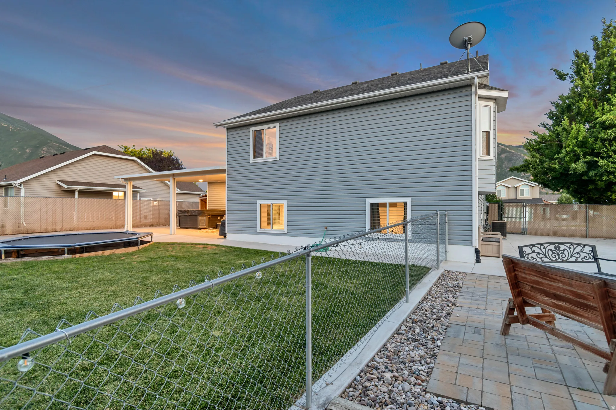 Expansive backyard featuring a chain-link fence, a covered patio area, and a large grassy lawn