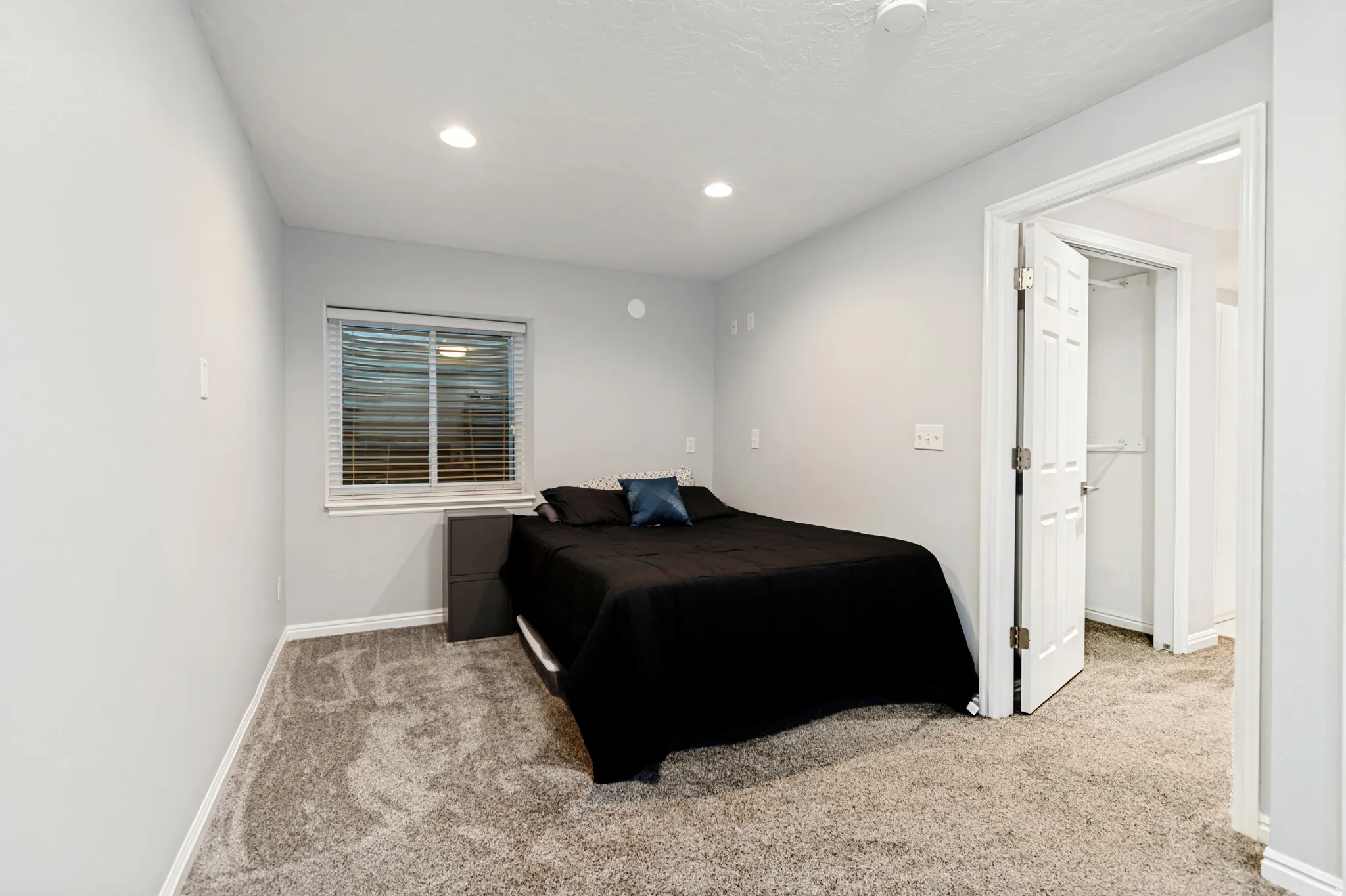 Bedroom featuring recessed lighting, light gray wall paint, a window with blinds, carpet flooring, and a white paneled door revealing a closet with shelving