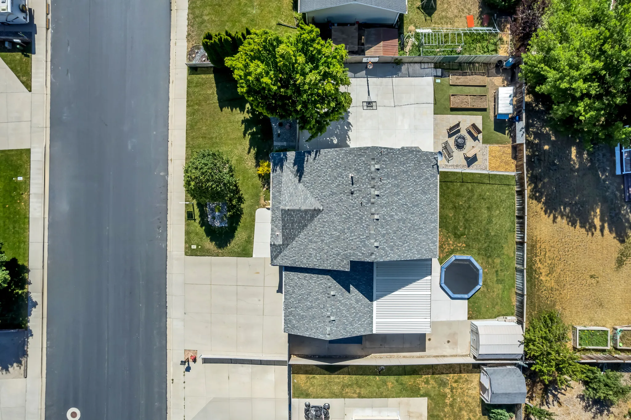 Aerial perspective showcasing a property with a gray shingle roof, extensive concrete driveway, and a spacious backyard