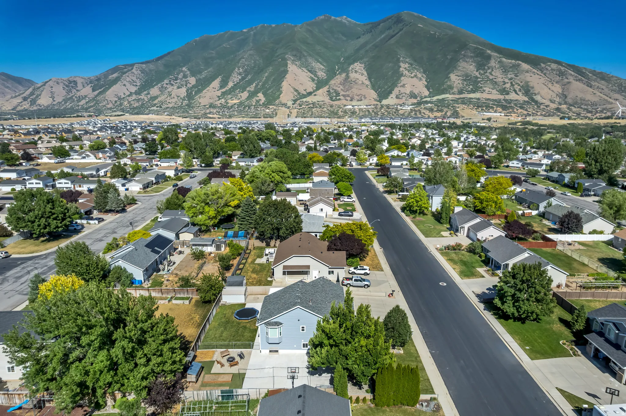 Suburban neighborhood featuring a paved street, mature trees, and mountain scenery