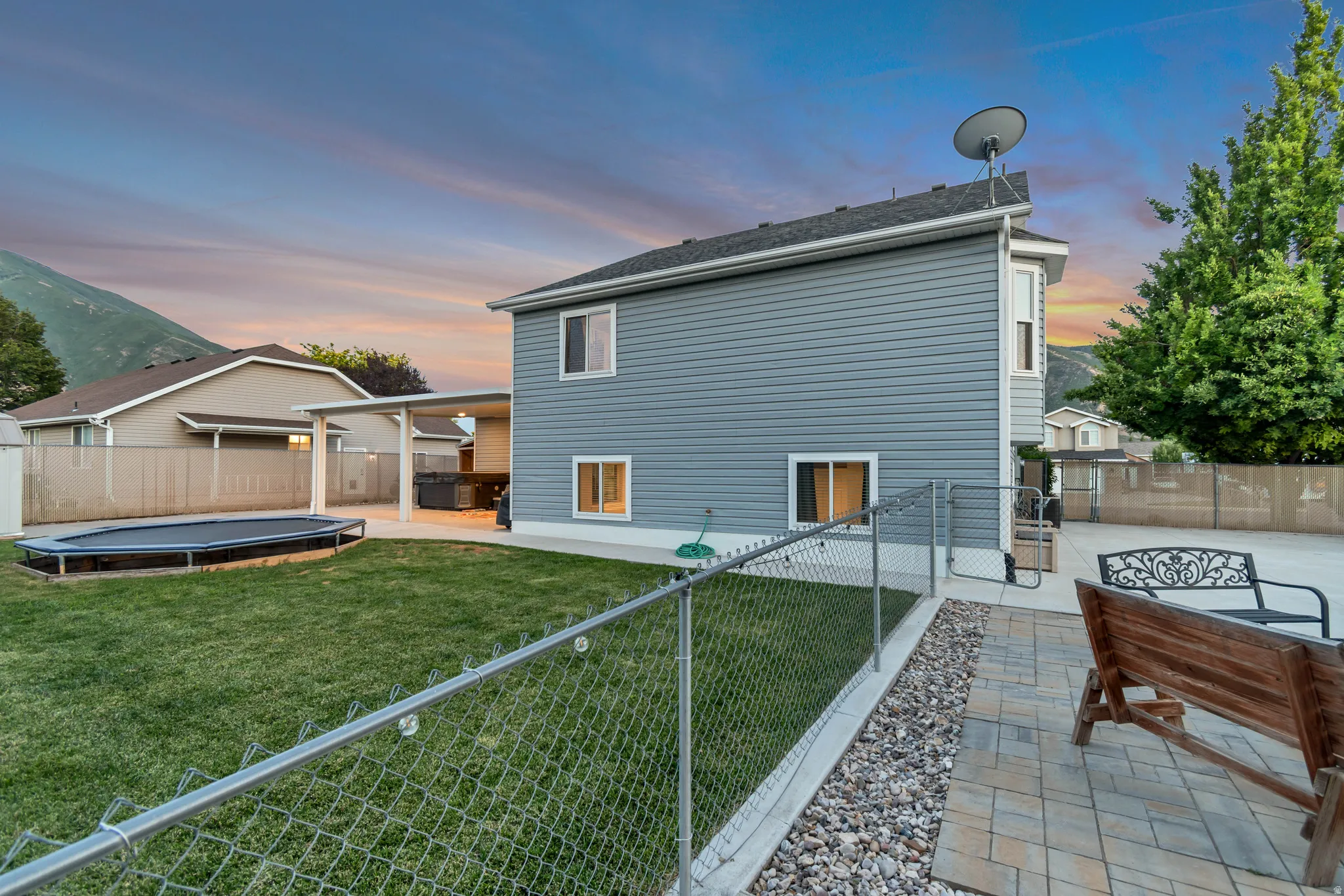 Expansive backyard featuring a lush lawn, chain-link fencing, and a paved patio area