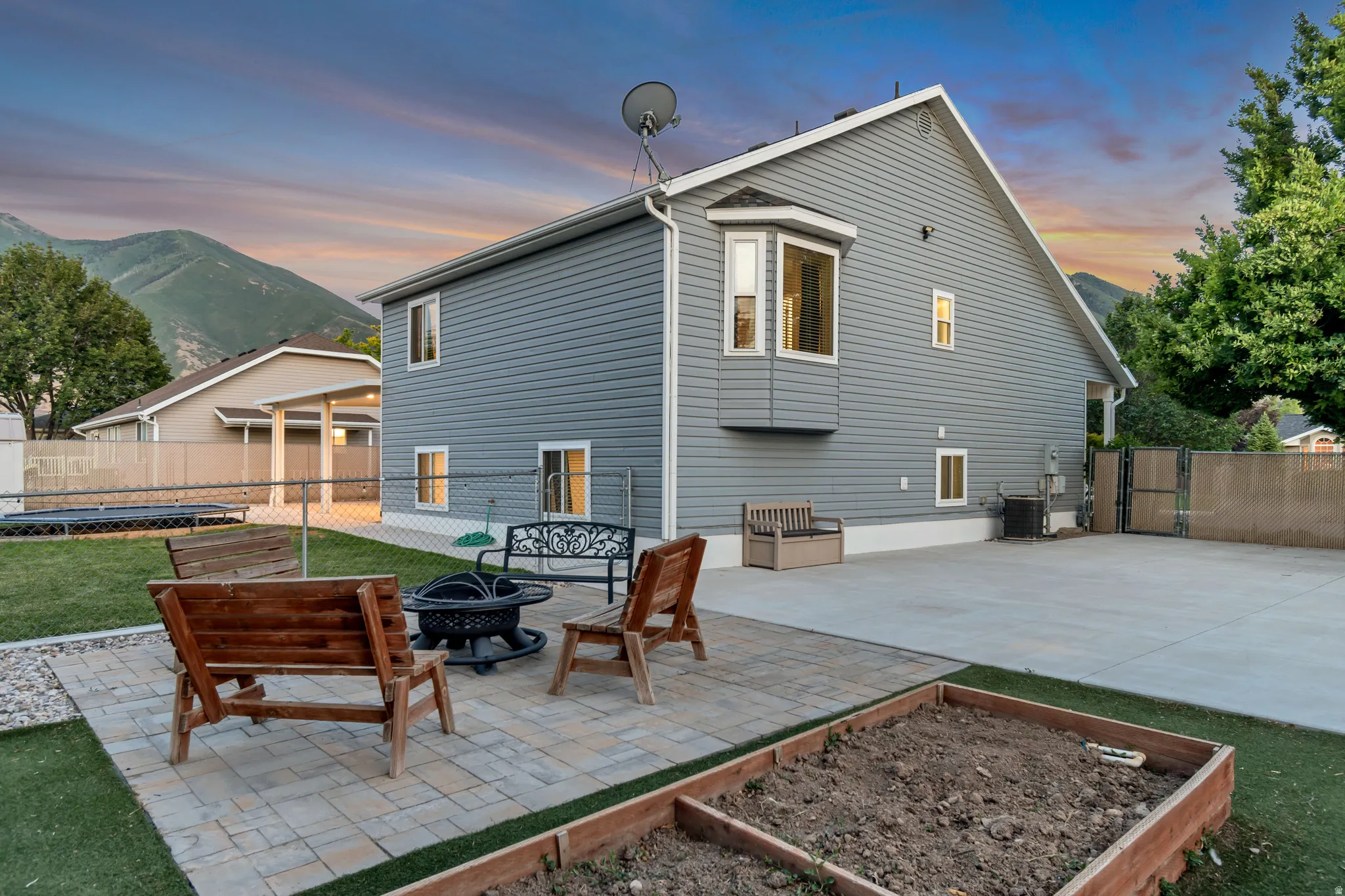 Expansive backyard featuring a paver patio with a built-in fire pit, a raised garden bed, and a sizable concrete pad
