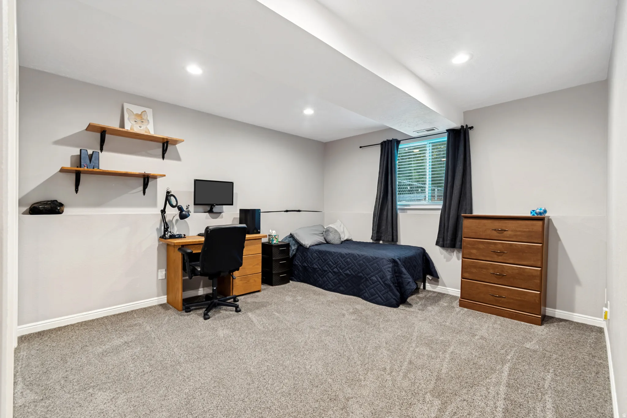 Spacious room featuring gray carpet, light gray walls with a chair rail, recessed lighting, and a single window with blinds and dark curtains
