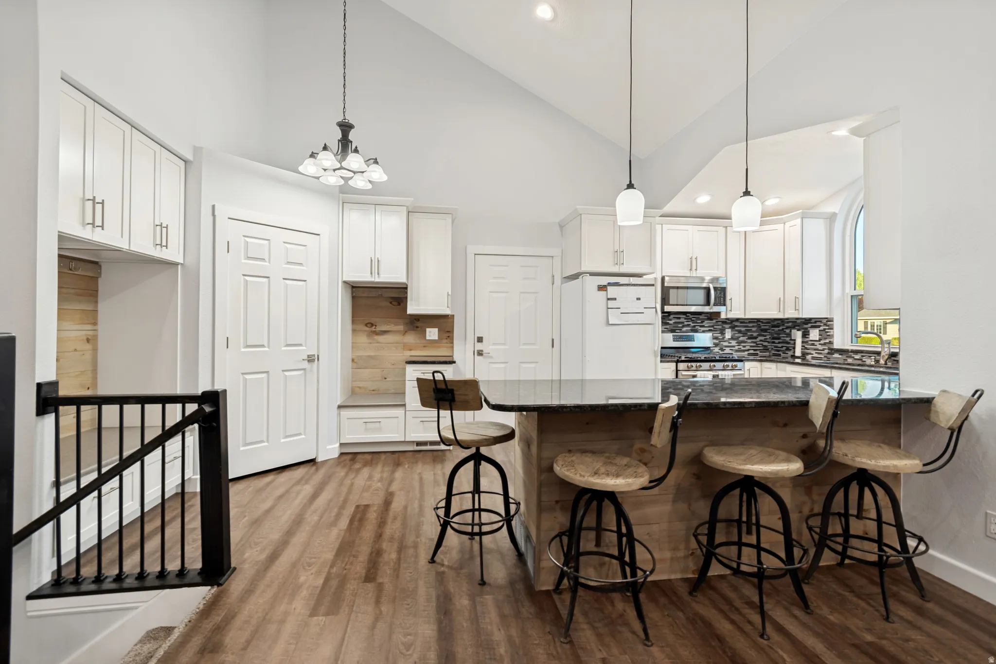 Kitchen featuring a waterfall-edge island with a dark countertop, white shaker cabinetry, a tile backsplash, and stainless steel appliances