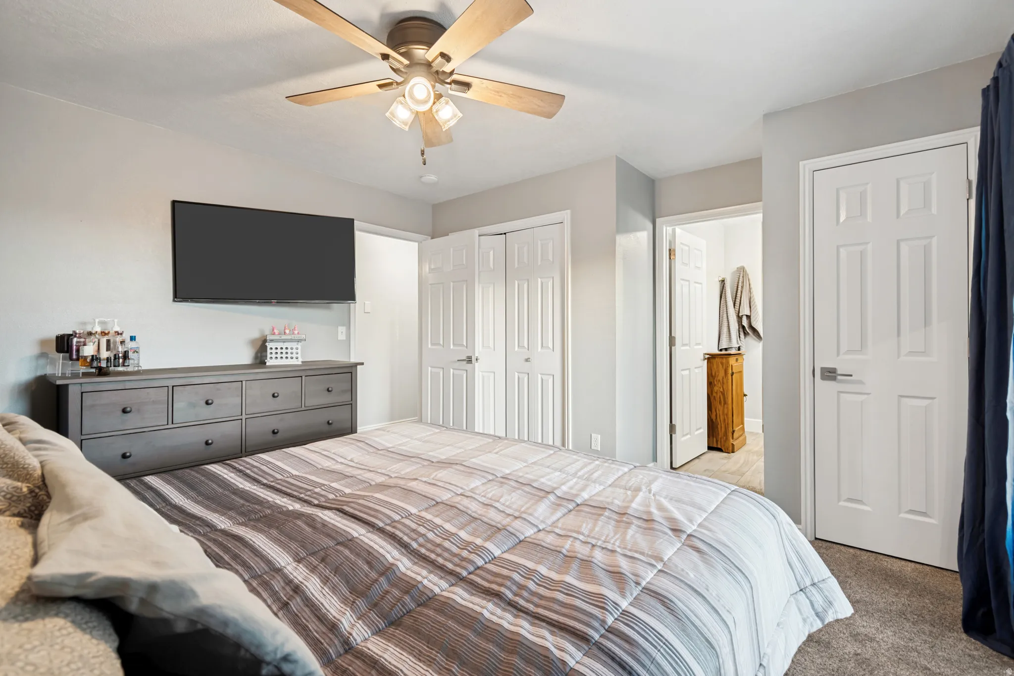 Neutral gray walls complement the carpeted flooring in this bedroom, featuring a ceiling fan with light fixture and multiple paneled doors