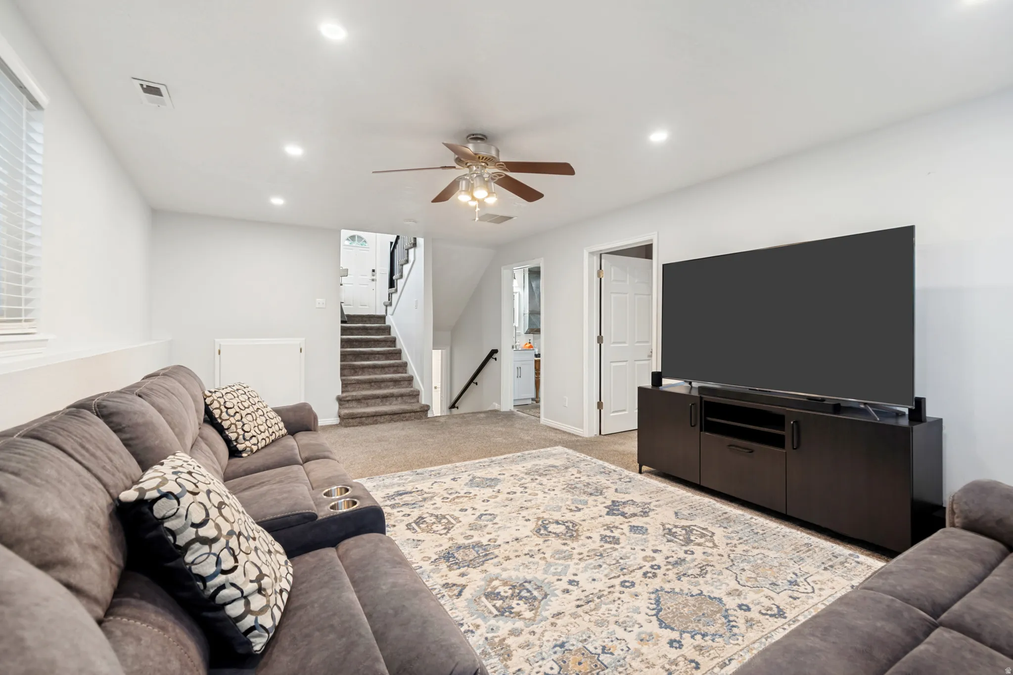 Spacious living area featuring neutral carpeting, recessed lighting, a ceiling fan, and a lower-level window with blinds