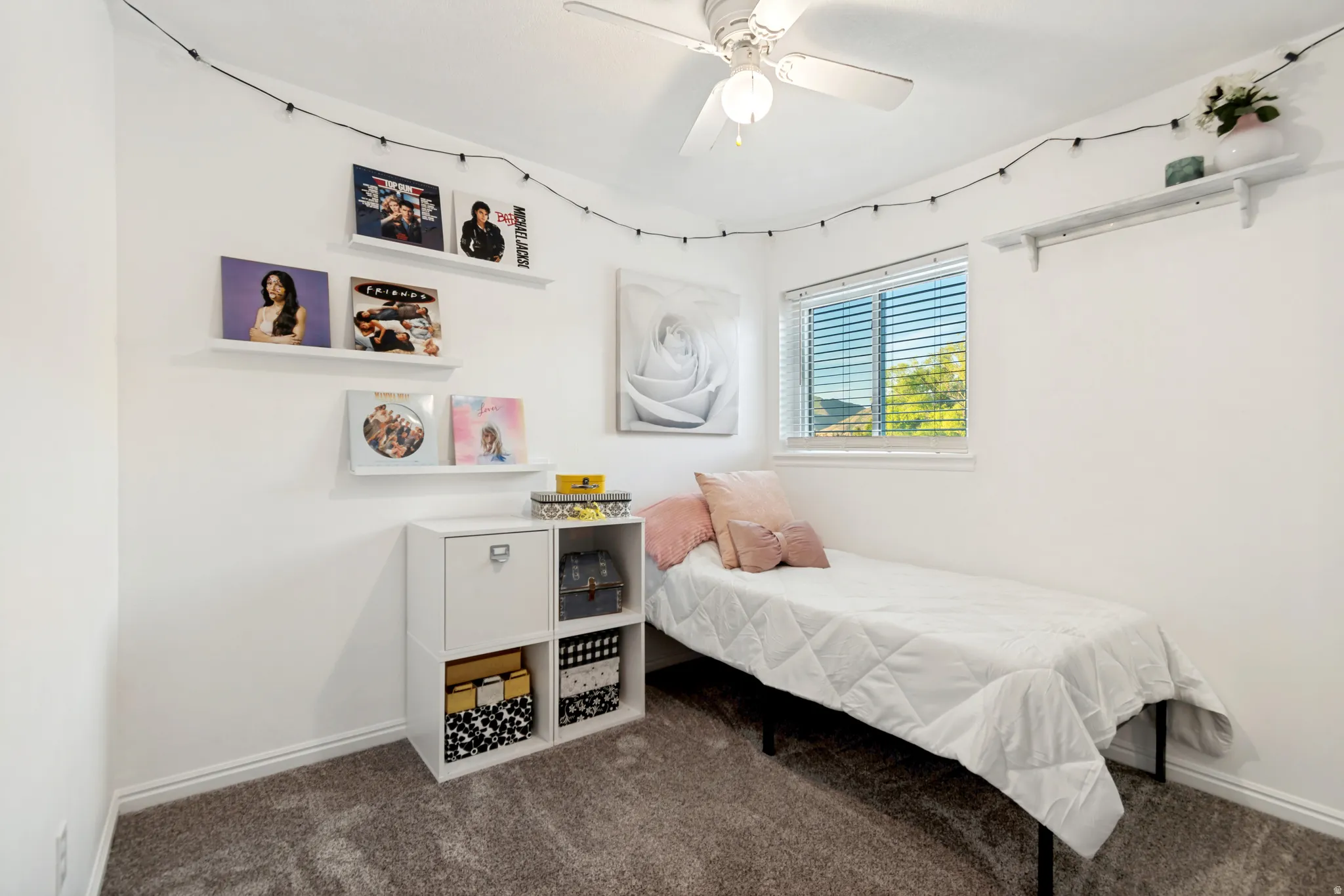 Bedroom featuring a ceiling fan, window with horizontal blinds, built-in wall shelving, and neutral carpeting