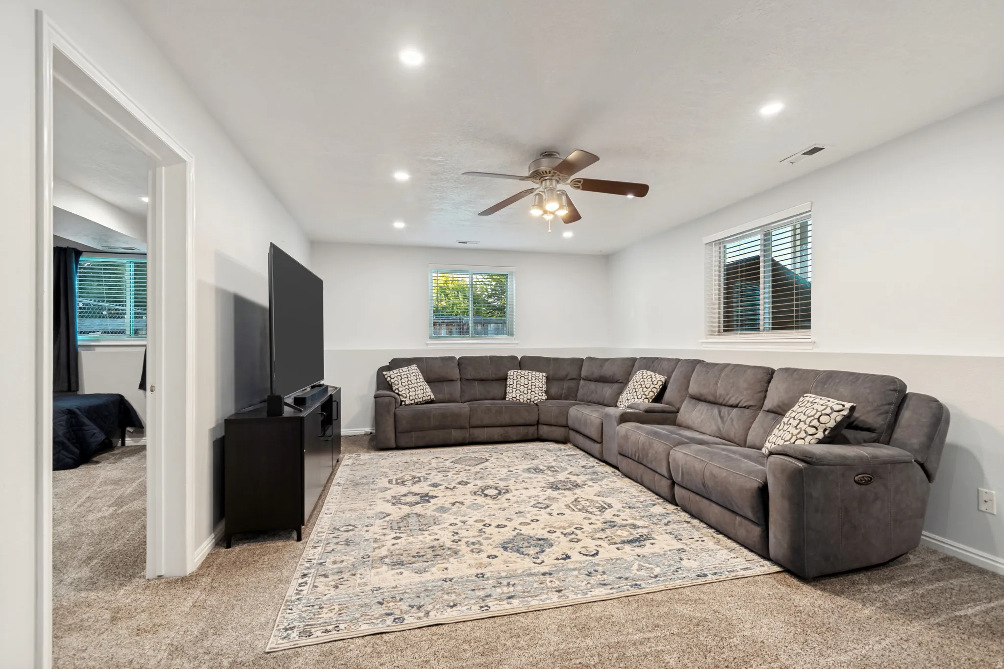 Spacious carpeted living area featuring recessed lighting, a ceiling fan, and multiple windows