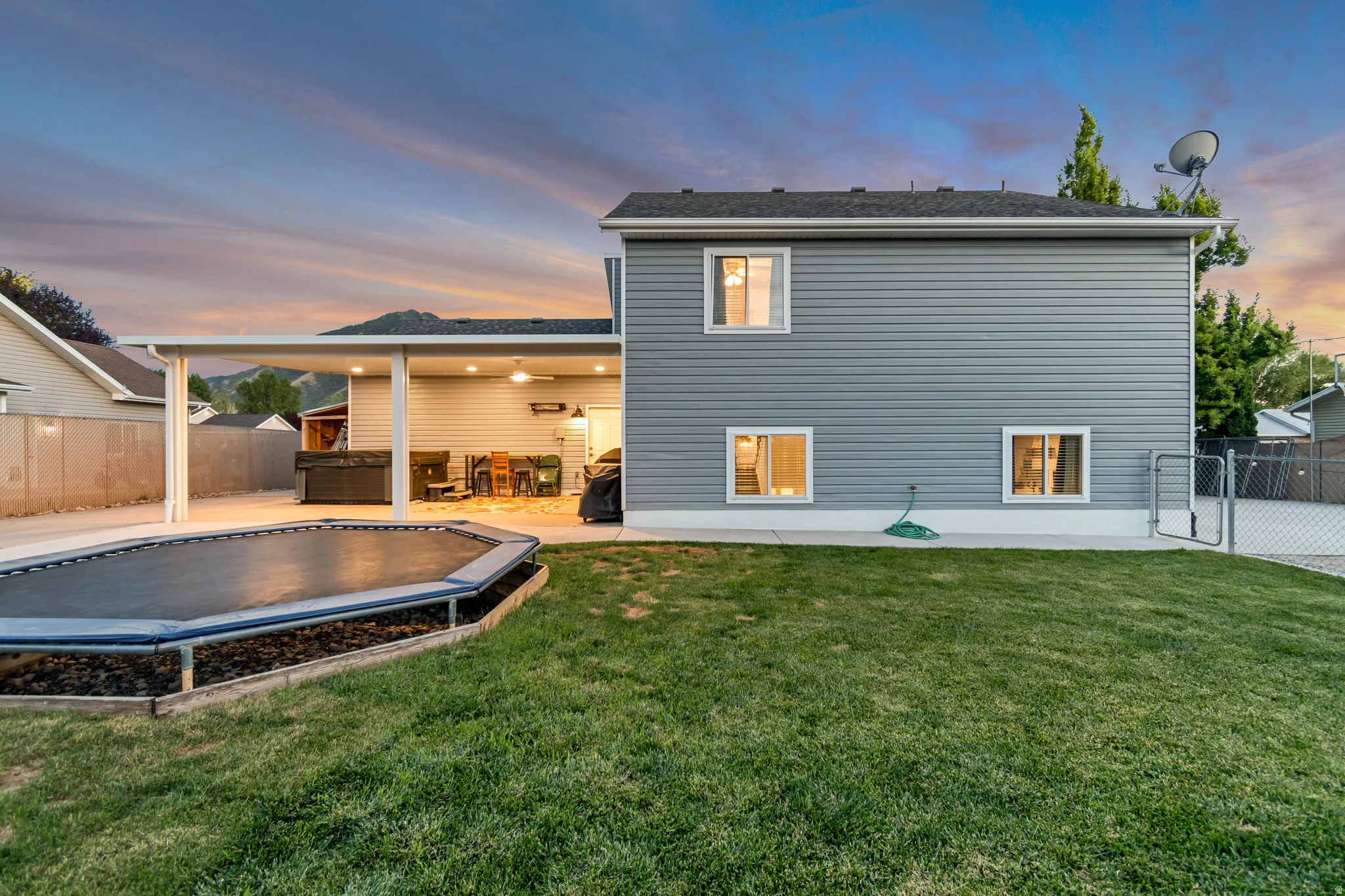 Expansive backyard featuring a manicured lawn, a large covered patio, and a chain-link fence