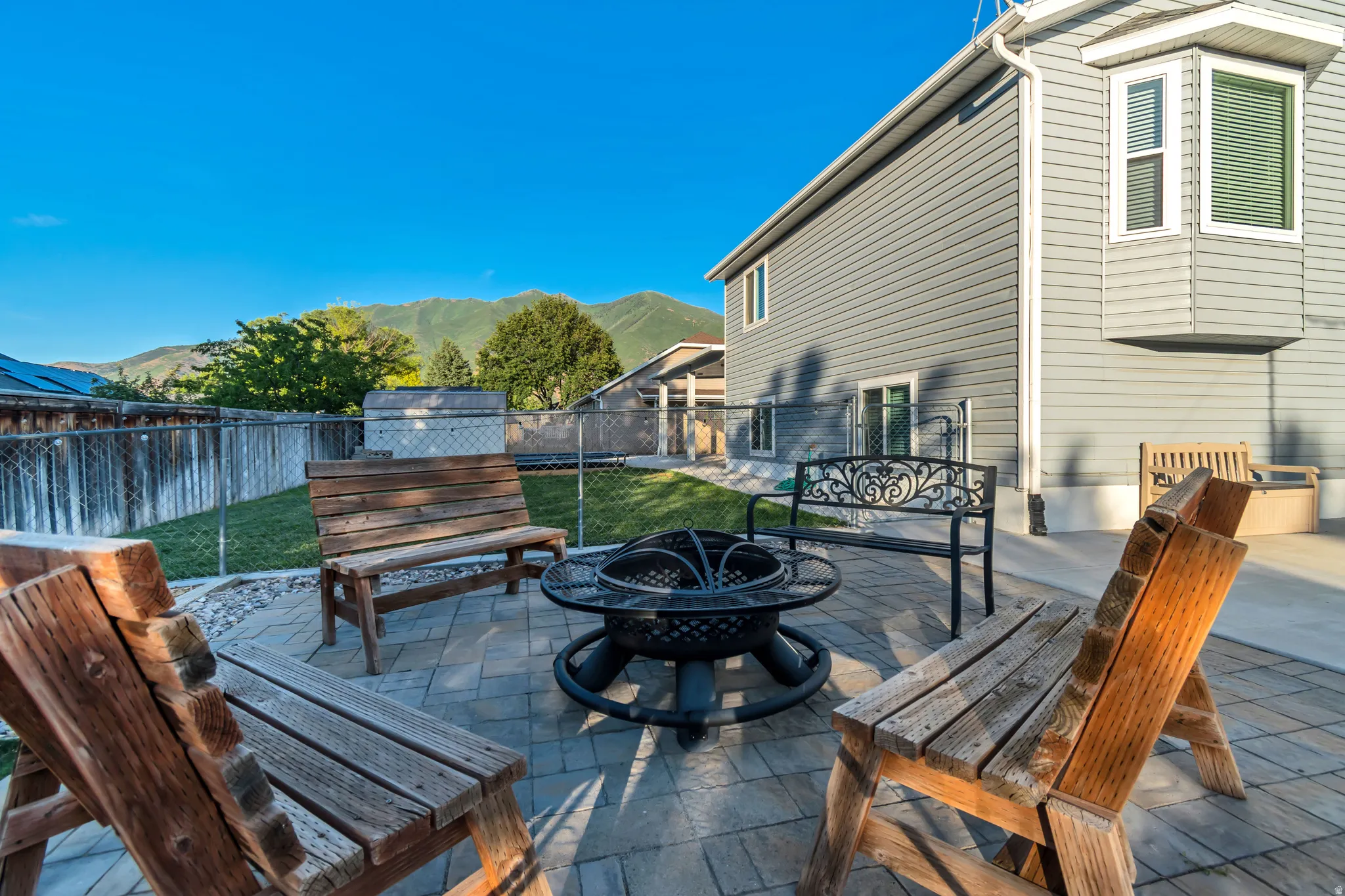 Backyard patio featuring a paver surface, integrated fire pit, and a chain link fence