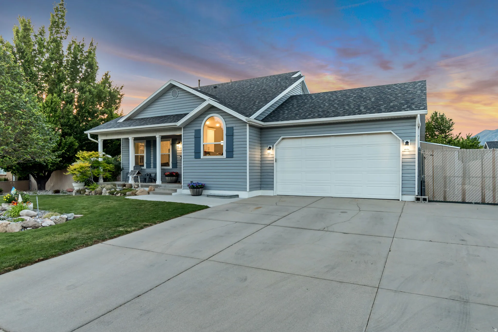 Light blue siding exterior featuring a covered porch, an arched window with blue shutters, a paved driveway, and a two-car garage
