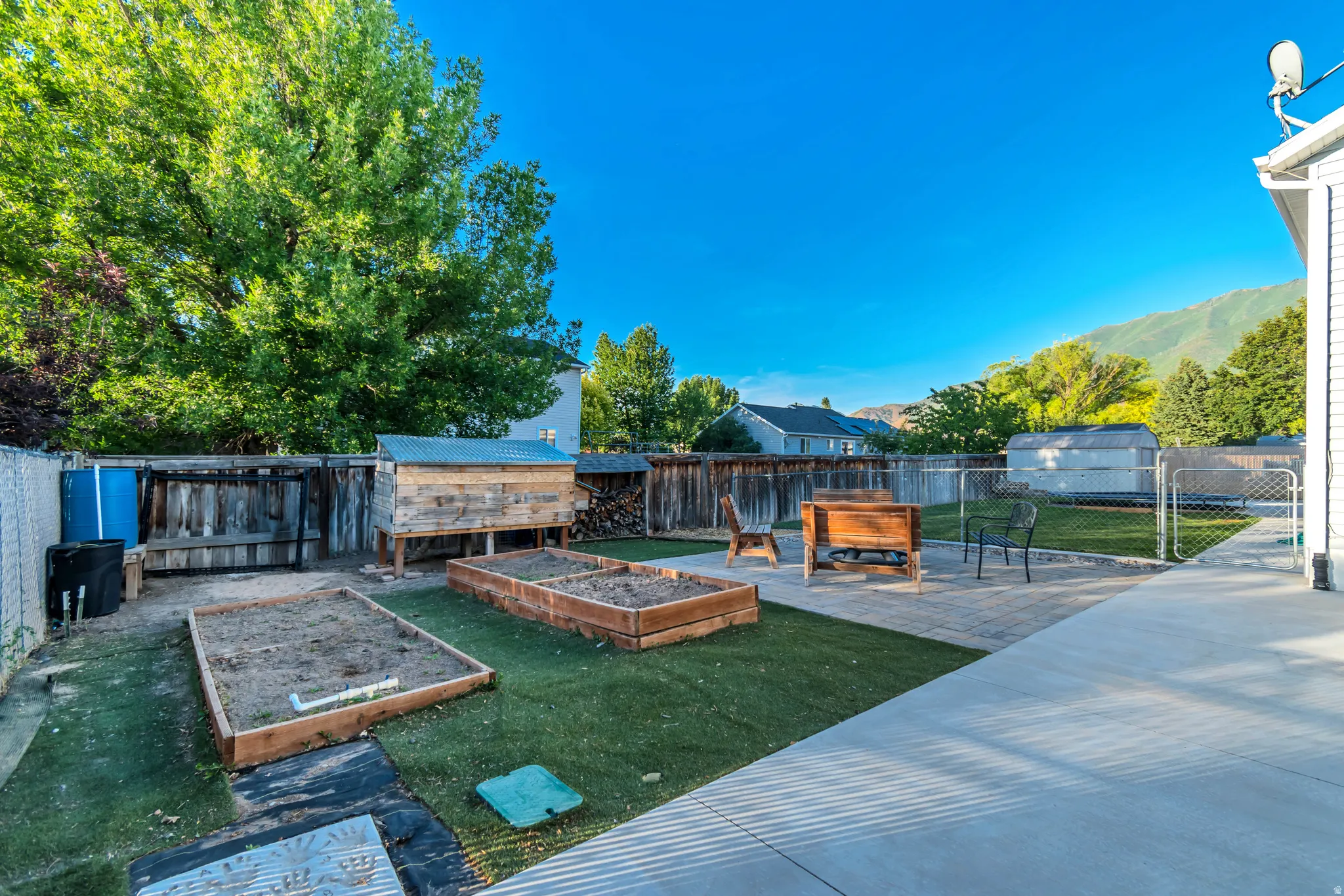 Expansive backyard featuring a concrete patio, artificial turf, and two raised garden beds