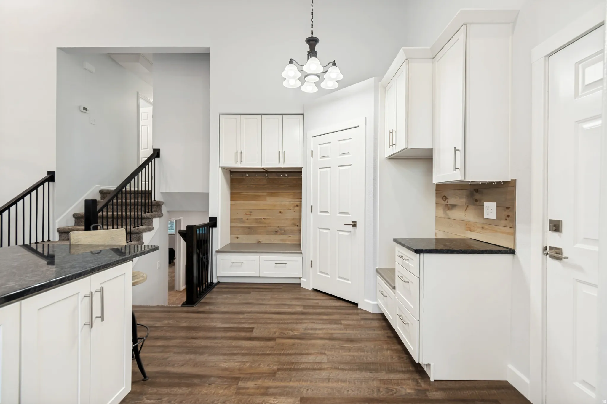 Entryway featuring built-in white cabinetry, wood-finish flooring, dark stone countertops, and a staircase with black railings