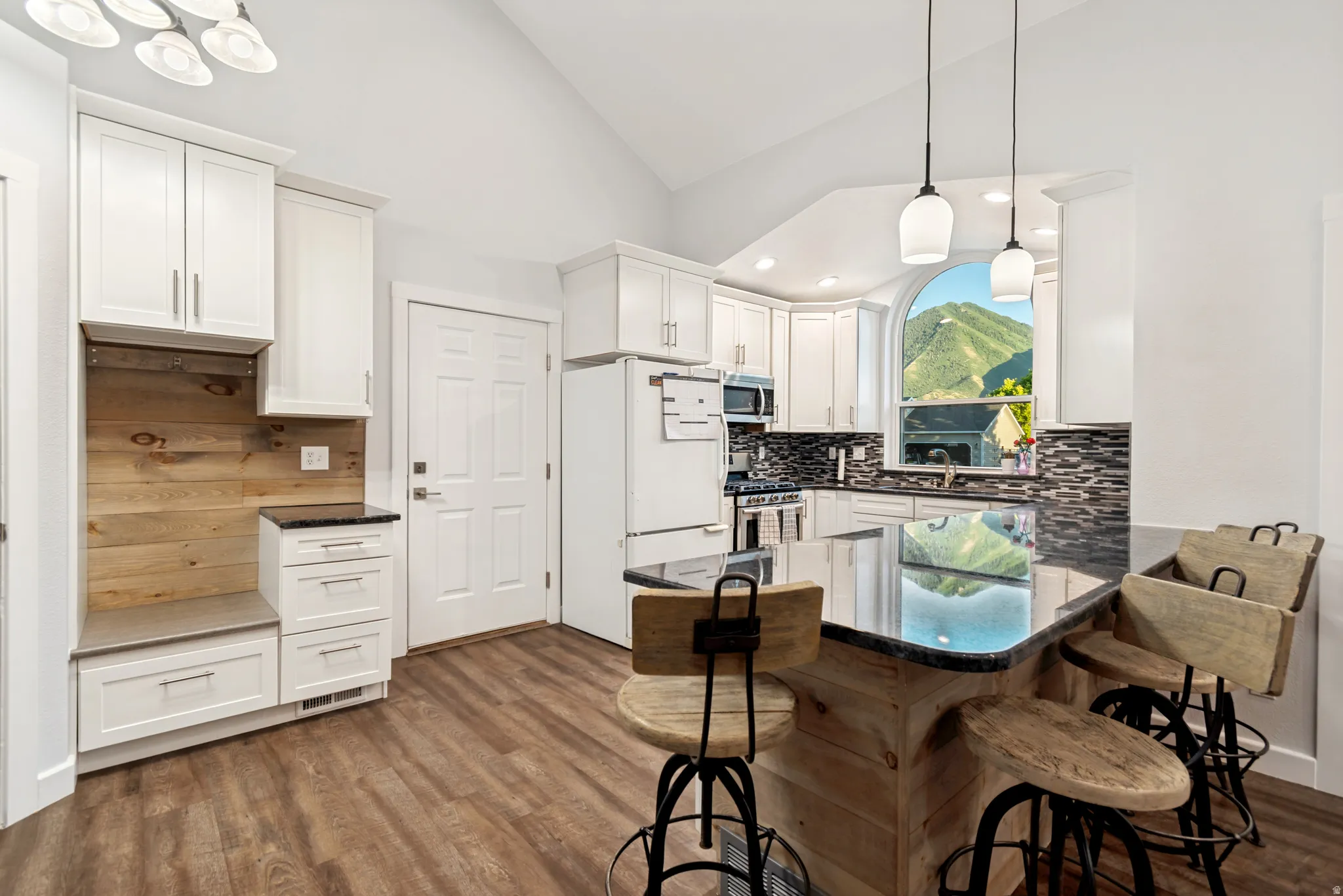 Kitchen featuring a multi-tone tile backsplash, white cabinetry, dark stone countertops, an arched window, and wood-finish flooring