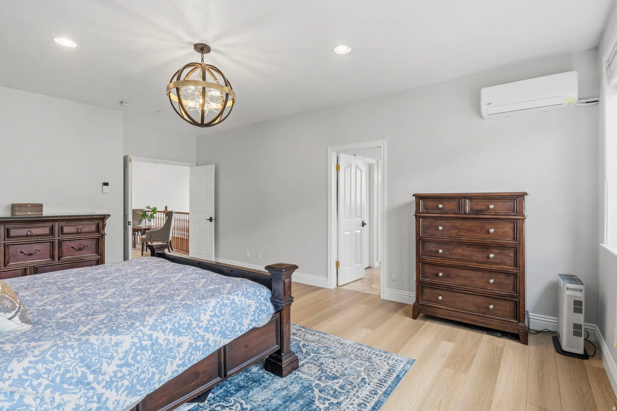 Bedroom featuring light wood-finish flooring, a contemporary spherical chandelier, recessed lighting, and a wall-mounted mini-split HVAC unit
